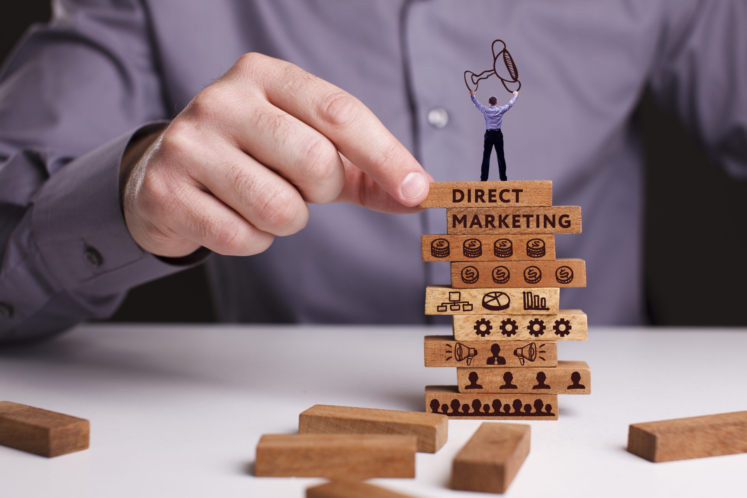 A person stacks blocks labeled “Direct Marketing,” symbolizing direct marketing success.